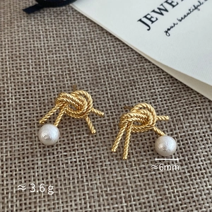 Macro detail of gold knotted metal earrings with 6mm white pearl drops and retro design