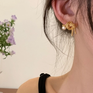 Detail of gold knotted stud earring with a round white pearl on a model ear
