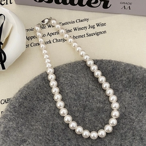 Gros plan d'un collier de perles blanches 8mm élégant avec fermoir argenté sur fond texturé