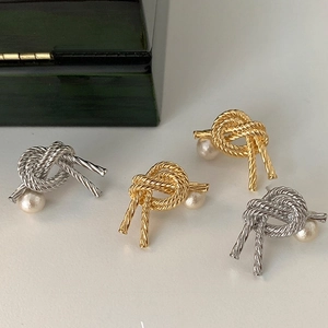 Detail of gold and silver knot earrings set featuring elegant faux pearls on white