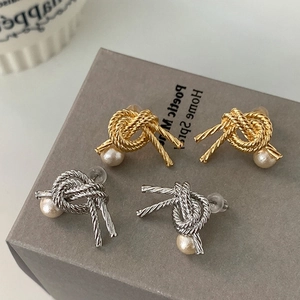 Detailed view of knot-shaped gold and silver earrings featuring creamy round pearls