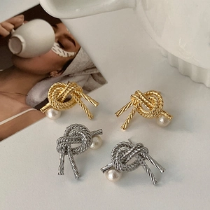 Detail of metal knot earrings with pearls in gold and silver finish on artistic background