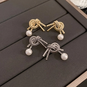 Vintage gold and silver knot earrings with white pearls displayed on a textured jewelry tray
