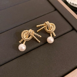 Detailed close-up of golden knot stud earrings with round white pearls on dark background