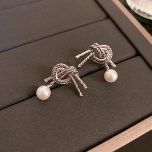 Close-up of knot design silver stud earrings with white pearls in a jewelry box