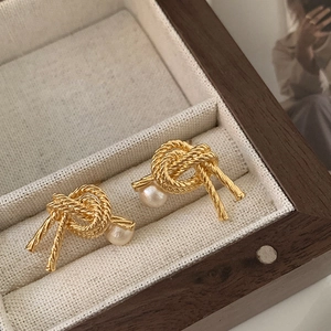 Detailed close-up of golden knot earrings with round white pearls in a wooden jewelry box