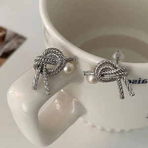 Macro detail of silver knot stud earrings with a single white pearl on a ceramic cup