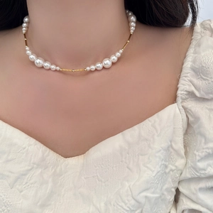Close-up of pearl necklace with gold metal tubes on woman neck over white dress