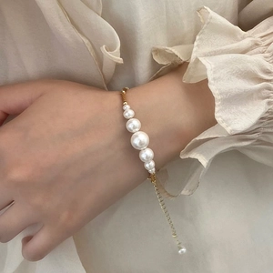 Close-up of elegant pearl bracelet with gold chain worn on wrist with chiffon blouse