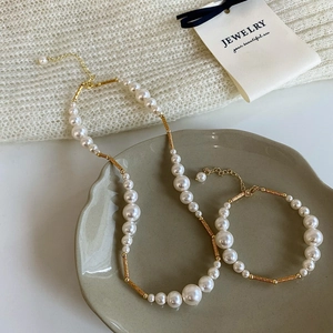 Elegant pearl necklace and bracelet set with gold metal tubes on a tray