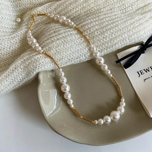 French retro pearl and gold metal tube necklace displayed on a ceramic jewelry tray