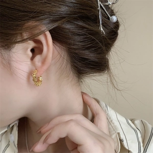 Détail de créoles dorées à texture grainée portées par un mannequin au style vintage
