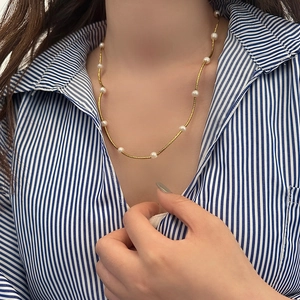 Detail of elegant gold-tone necklace with spaced freshwater pearls on a striped shirt