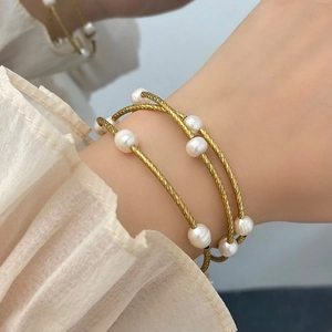 Detailed view of triple-layer gold wrap bracelet with lustrous white pearls and twisted metal