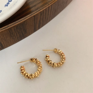 Détail de boucles d'oreilles dorées avec texture tissée sur fond blanc élégant