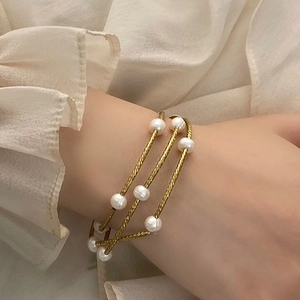 Detail of elegant gold layered bracelet with freshwater pearls on a cream blouse