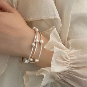 Close-up of three layered silver pearl bracelets worn on wrist over white chiffon