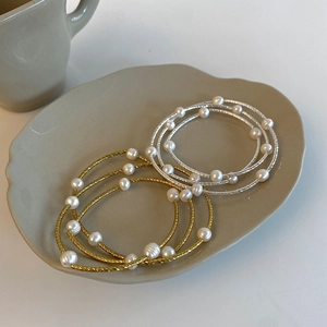 Detail of layered gold and silver twisted pearl bracelets on a ceramic plate