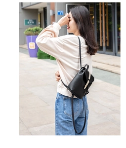 Outdoor street style view of a black leather mini backpack with metal buckle strap