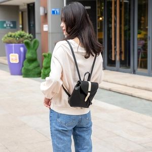 Minimalist black mini backpack with contrast cream strap and gold buckle in outdoor setting