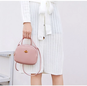 Détail du sac bandoulière rose rond avec emblème d'abeille dorée et poignée