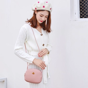 Détail du petit sac rond rose avec fermoir abeille dorée porté par un mannequin