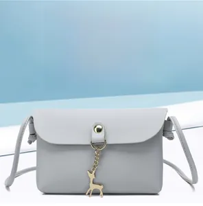 Detail of light grey mini crossbody bag with golden deer charm and magnetic snap closure