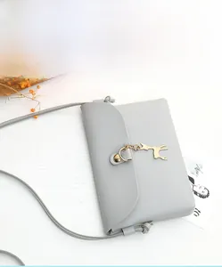 Detail of grey pebble leather mini crossbody bag with a metal deer charm and flap closure