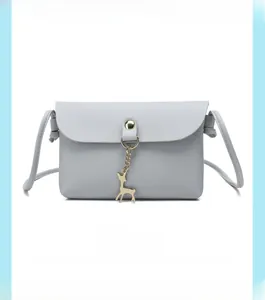 Detail of light gray PU leather crossbody bag with golden deer charm and snap closure
