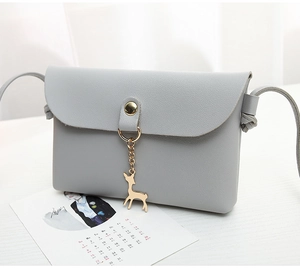 Close-up of grey leather crossbody bag featuring a golden deer charm and metal buckle