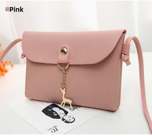 Close-up of pink mini crossbody bag with gold deer pendant on a white wooden table