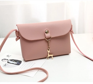 Detailed close-up of pink textured leather crossbody bag with a gold deer pendant
