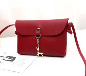 Close-up of red crossbody bag with golden deer pendant and fine litchi texture