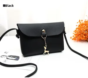Detail view of black faux leather crossbody bag with golden deer charm on white background