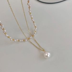 Detail of double-layer pearl necklace featuring golden beads and a large pearl pendant