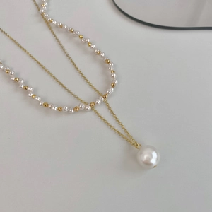 Elegant layered pearl necklace with gold chain and large white pearl pendant on gray base