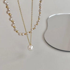 Detail of double-layer gold plated necklace with pearls on a minimalist mirror surface