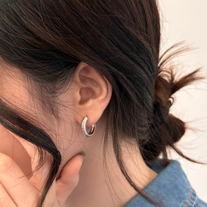 Macro close-up of textured silver hoop earrings with twisted thread pattern on a model