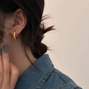 Close-up of golden vintage textured hoop earring with vertical threaded design on model