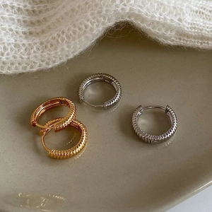 Elegant gold and silver twisted ribbed hoop earrings displayed on a ceramic plate