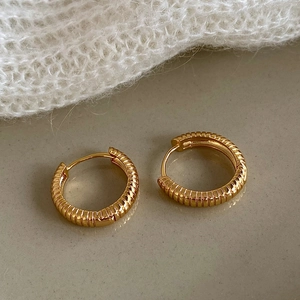 Close-up of golden hoop earrings with fine vertical grooves on a stone surface