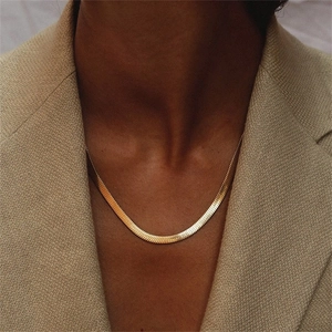 Close-up of a sleek golden herringbone snake chain necklace on a female model