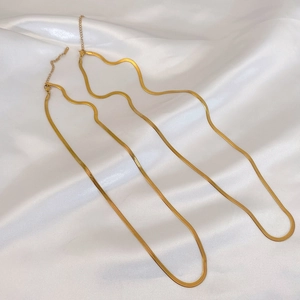 Flat gold snake bone chain necklace layered on white satin fabric background