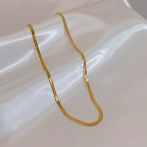 Close-up of golden flat snake chain necklace on white silk fabric background