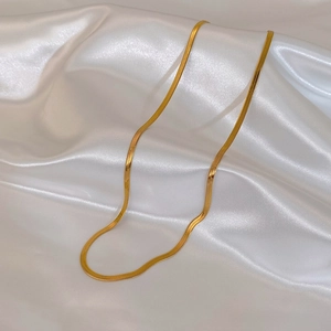 Close-up of a sleek gold flat snake chain necklace on white silk fabric background