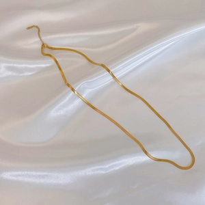 Close-up of gold snake bone chain necklace lying on white satin fabric background