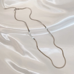 Macro shot of silver snake bone chain with lobster clasp on elegant white satin fabric