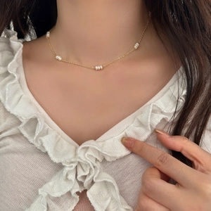Détail d'un collier en chaîne dorée avec perles d'eau douce porté par un mannequin
