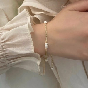 Détail d'un bracelet fin doré avec des perles porté délicatement au poignet d'une femme