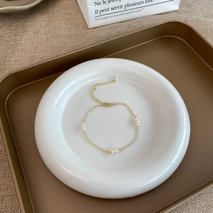 Détail macro d'un bracelet doré avec perles d'eau douce sur une assiette blanche